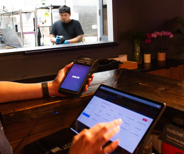 Staff using Oolio POS and payments with kitchen pass in the background